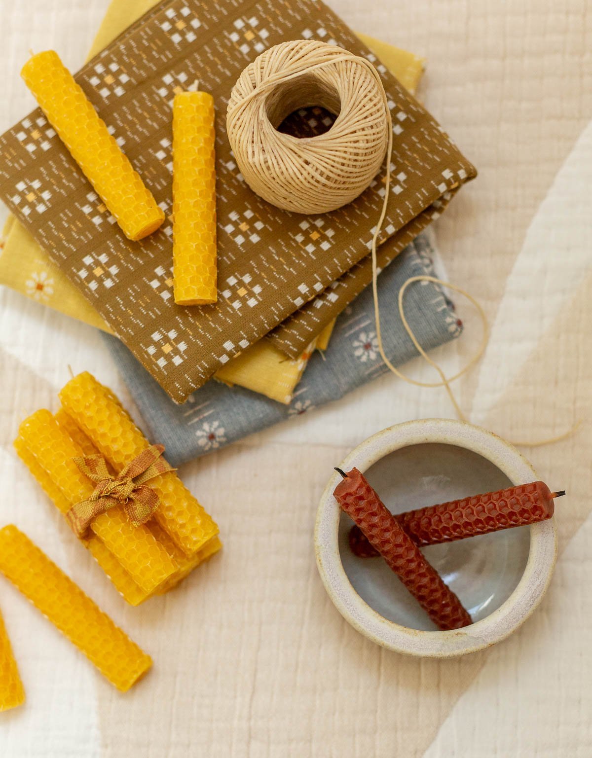 rolled candles on a crafting surface with fabric and candle wicks