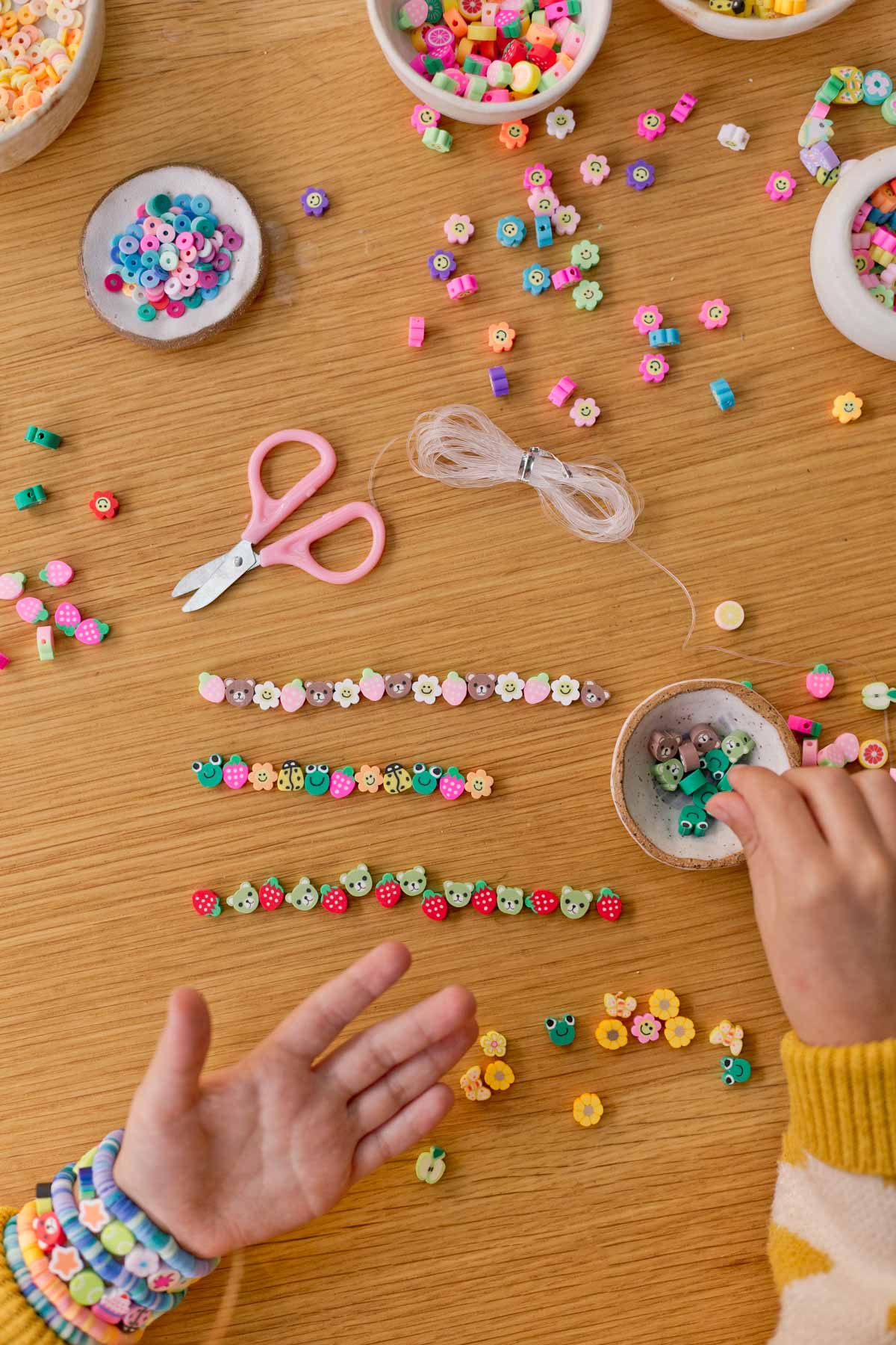 child putting together bracelets with polymer clay beads on a flat wood surface